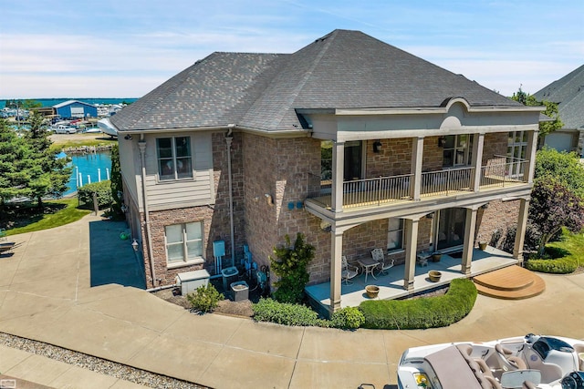 exterior space featuring stone siding, a patio, a balcony, and a water view