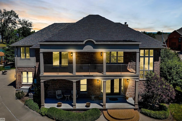 back of house at dusk with a patio, a balcony, and stone siding