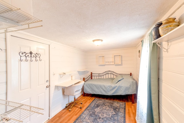 bedroom with wood-type flooring, wooden walls, and a textured ceiling