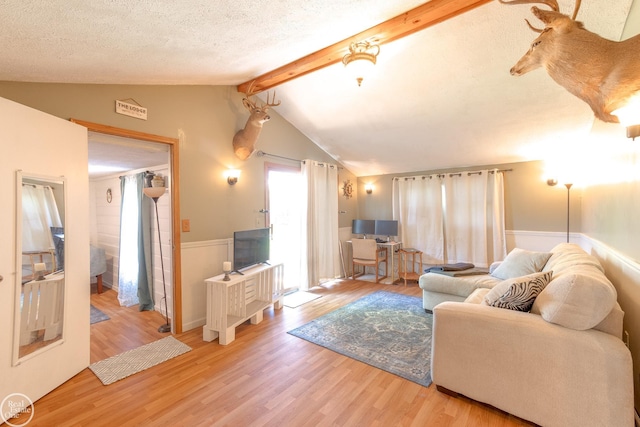 living room featuring lofted ceiling with beams, light hardwood / wood-style floors, and a textured ceiling