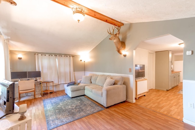 living room featuring vaulted ceiling with beams, a textured ceiling, and light hardwood / wood-style flooring