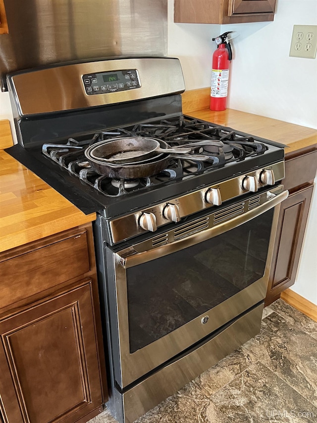 kitchen with dark brown cabinetry, butcher block countertops, and stainless steel gas stove