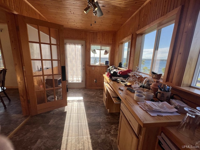 interior space featuring a water view, wooden ceiling, ceiling fan, and wood walls