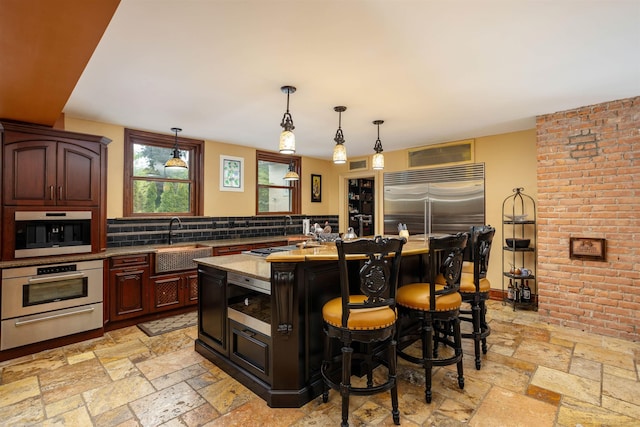 kitchen featuring sink, a kitchen breakfast bar, light stone counters, built in appliances, and a kitchen island with sink