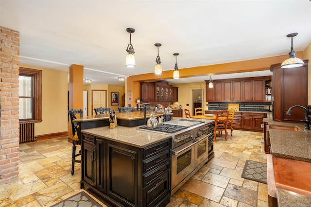 kitchen featuring dark brown cabinetry, sink, pendant lighting, range with two ovens, and a kitchen island with sink