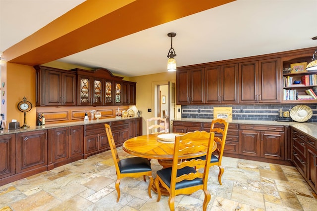 kitchen featuring light stone countertops, dark brown cabinets, backsplash, and hanging light fixtures