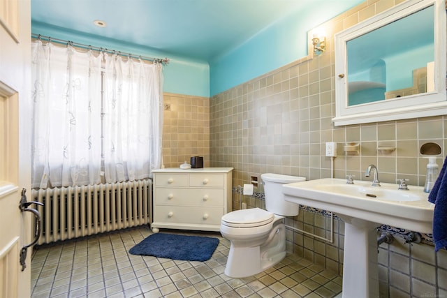 bathroom with radiator, sink, tile patterned flooring, toilet, and tile walls