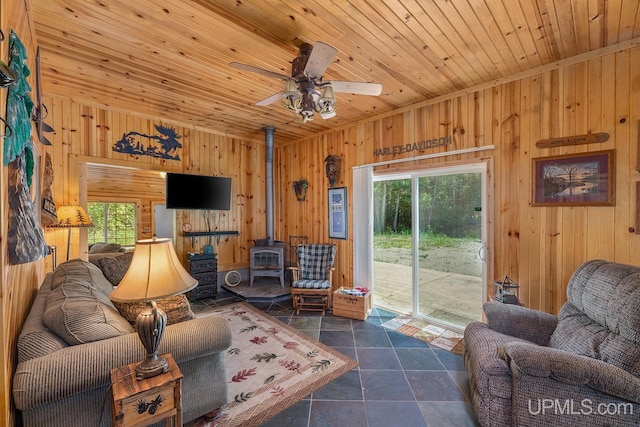 tiled living room with wooden walls, wooden ceiling, a wood stove, and a healthy amount of sunlight