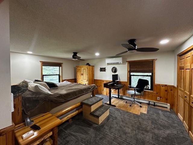 bedroom with a closet, a wall mounted AC, baseboard heating, ceiling fan, and wood-type flooring