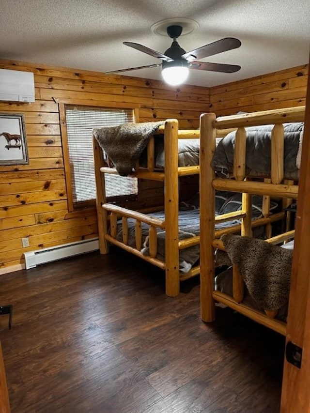 bedroom with wooden walls, a baseboard heating unit, a textured ceiling, dark wood-type flooring, and ceiling fan