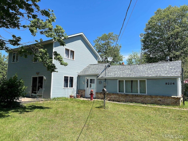 rear view of property featuring brick siding, a shingled roof, and a yard