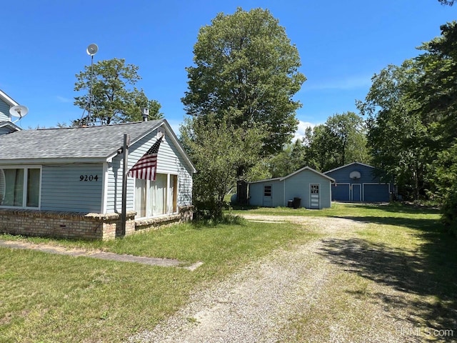 view of side of property with roof with shingles, a yard, and driveway