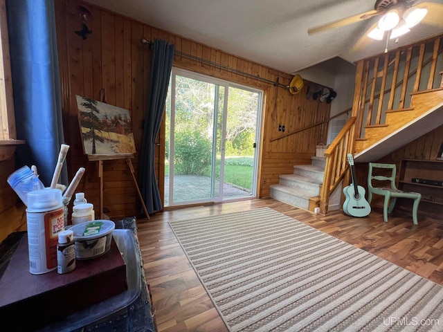 living room featuring wooden walls, a ceiling fan, stairway, wood finished floors, and a textured ceiling