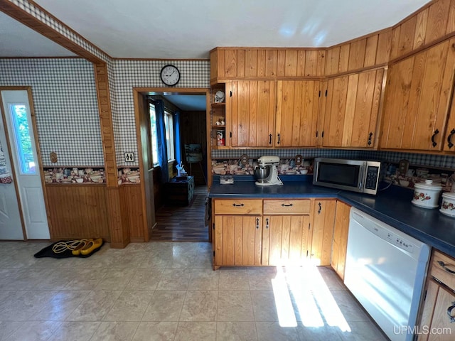 kitchen featuring dark countertops, wallpapered walls, white dishwasher, and stainless steel microwave