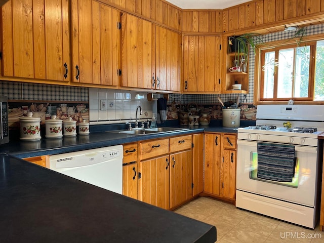 kitchen with white appliances, backsplash, dark countertops, and a sink