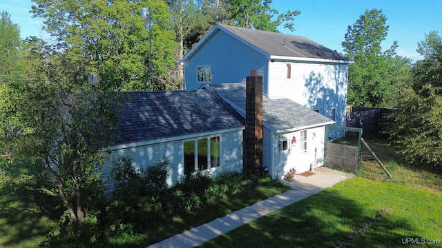 exterior space featuring a shingled roof, a yard, a chimney, and fence