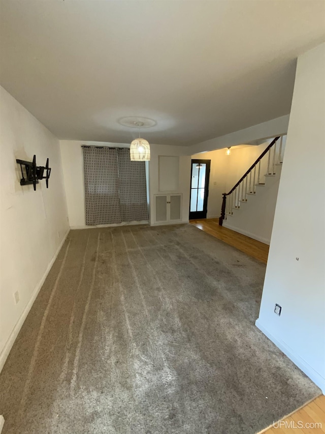 unfurnished living room with carpet floors, stairs, and baseboards