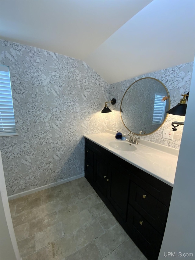 bathroom with vaulted ceiling, vanity, baseboards, and wallpapered walls