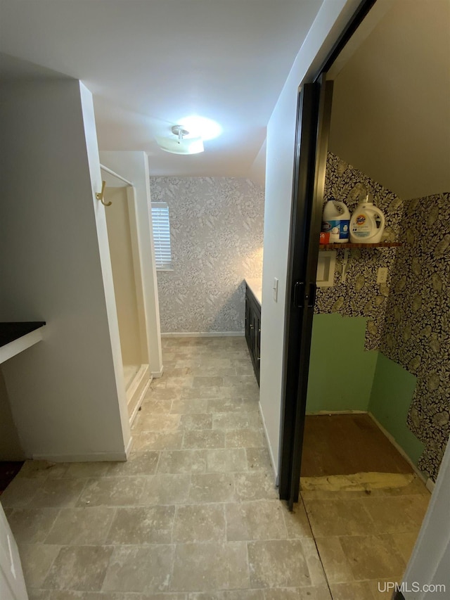 full bathroom with stone finish flooring, a shower stall, and wallpapered walls