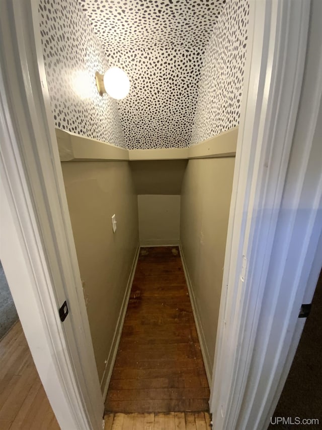 corridor featuring wood-type flooring, vaulted ceiling, and baseboards