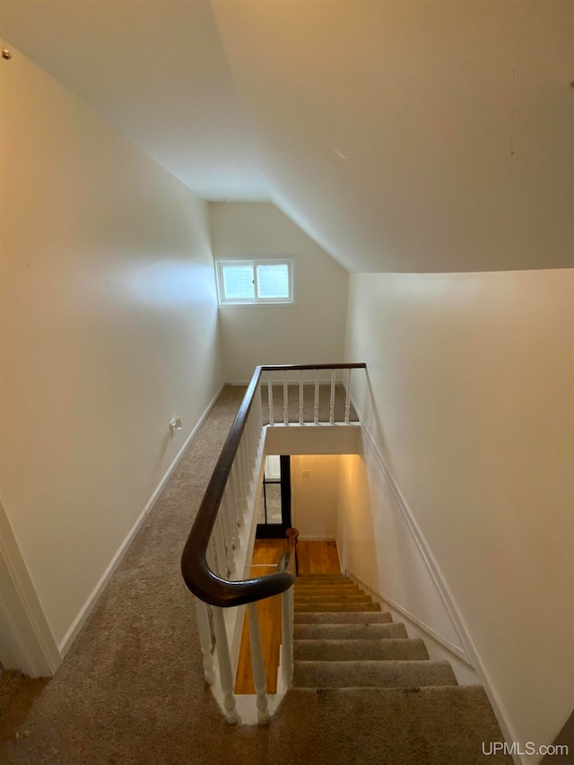 stairway with lofted ceiling and dark colored carpet