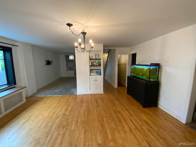 unfurnished living room featuring light hardwood / wood-style flooring, radiator heating unit, and an inviting chandelier