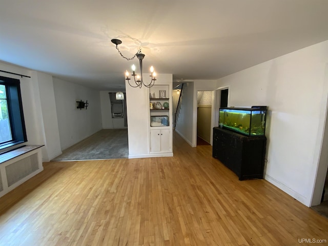 unfurnished dining area with light wood-style floors, stairway, radiator heating unit, and an inviting chandelier