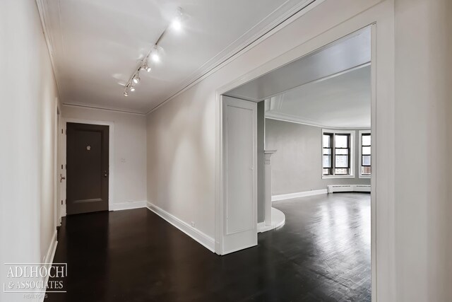 corridor featuring crown molding, dark hardwood / wood-style floors, a baseboard radiator, and rail lighting