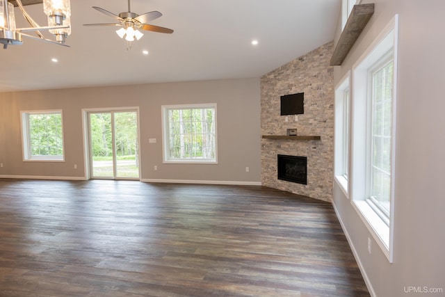 unfurnished living room featuring a stone fireplace, ceiling fan with notable chandelier, dark hardwood / wood-style flooring, and high vaulted ceiling