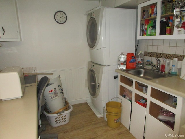 laundry room featuring stacked washing maching and dryer, light hardwood / wood-style flooring, sink, and wooden walls