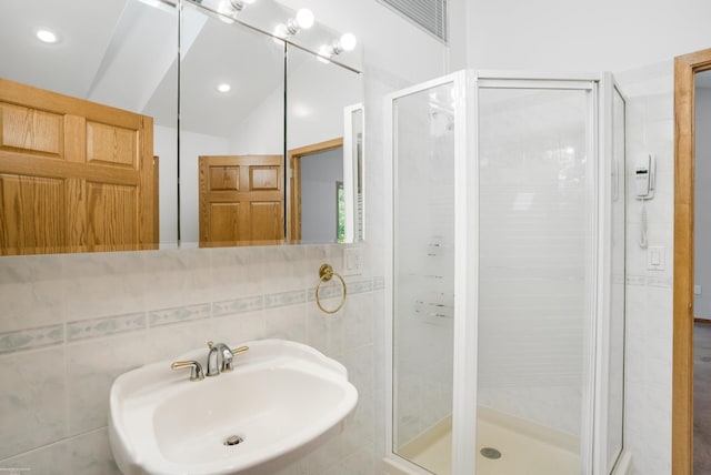 bathroom with a shower with door, sink, vaulted ceiling, tile walls, and tasteful backsplash