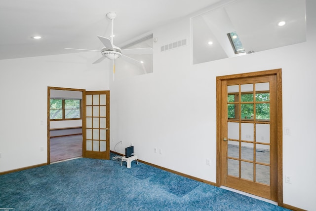 empty room featuring vaulted ceiling with skylight, ceiling fan, carpet floors, and french doors