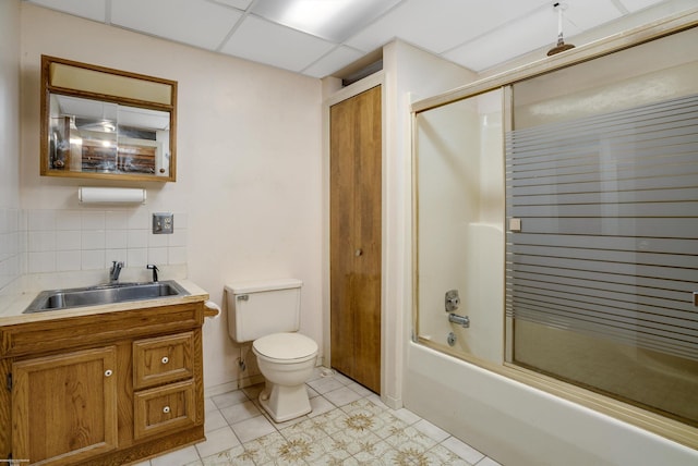 full bathroom featuring a drop ceiling, tile patterned floors, combined bath / shower with glass door, decorative backsplash, and toilet