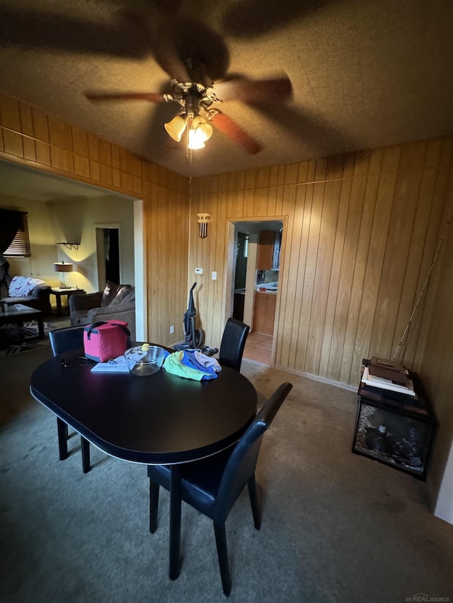 carpeted dining area featuring a ceiling fan and wooden walls