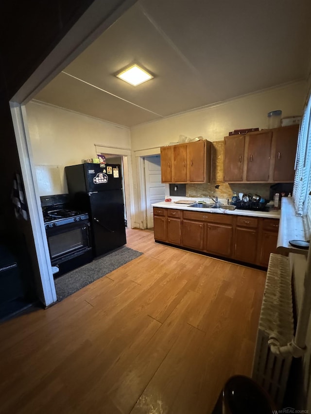 kitchen with light wood finished floors, decorative backsplash, brown cabinetry, freestanding refrigerator, and a sink