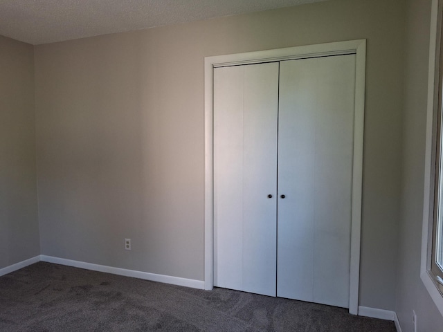 unfurnished bedroom with a closet, a textured ceiling, and dark colored carpet