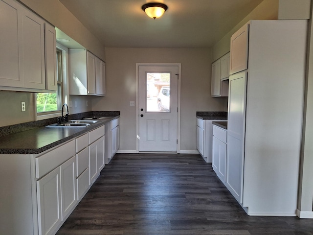 kitchen with dark countertops, dark wood finished floors, white cabinets, and a sink