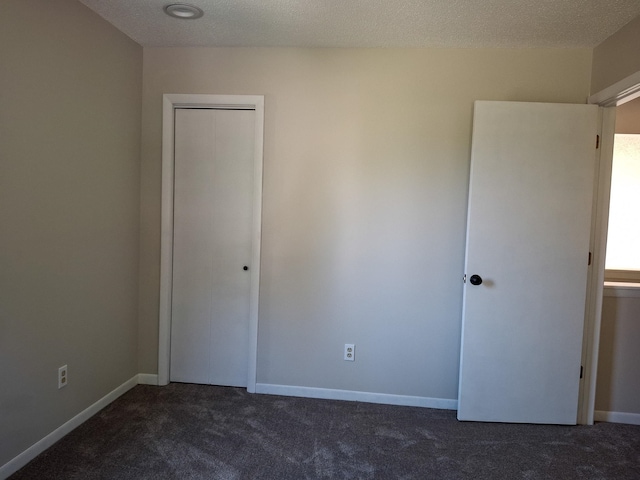 unfurnished bedroom with dark carpet, a closet, and a textured ceiling