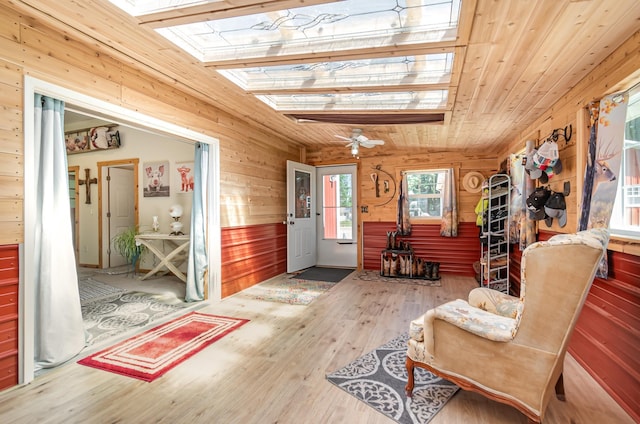 living area with a skylight, wood ceiling, ceiling fan, wooden walls, and hardwood / wood-style floors