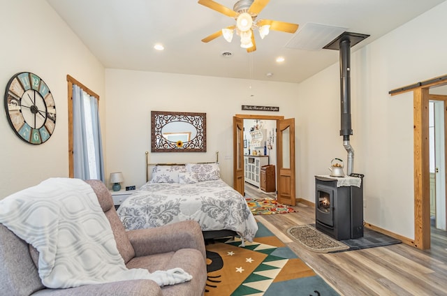 bedroom with a wood stove, ceiling fan, and hardwood / wood-style flooring