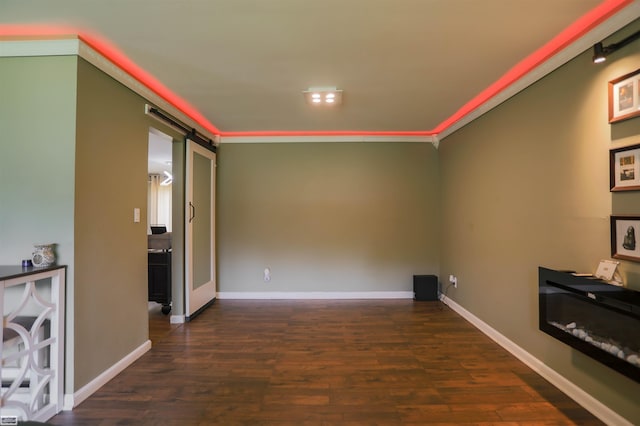 unfurnished living room with crown molding, baseboards, dark wood finished floors, and a barn door