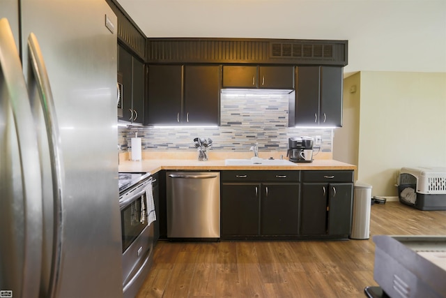 kitchen featuring a sink, appliances with stainless steel finishes, decorative backsplash, and dark wood-style floors