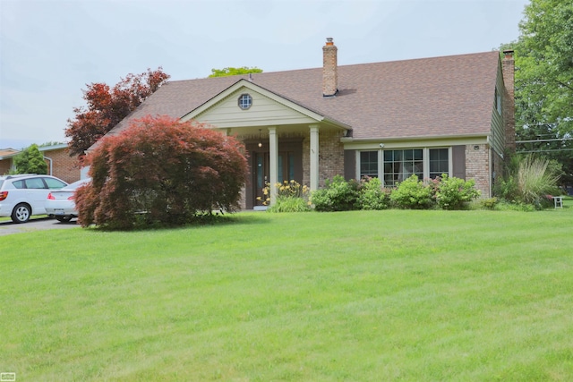 view of front of home with brick siding, a shingled roof, a front lawn, and a chimney