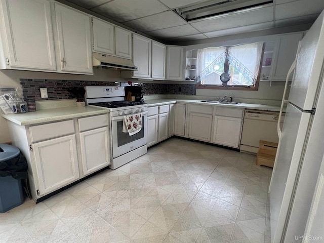 kitchen with a drop ceiling, backsplash, sink, white appliances, and white cabinetry