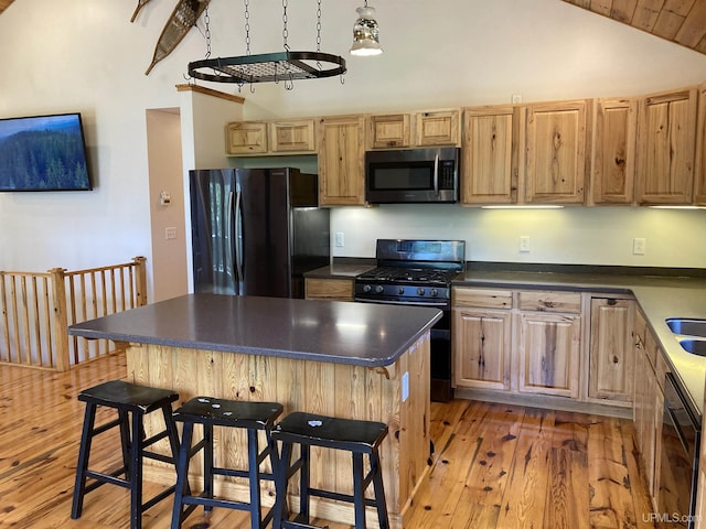 kitchen with dark countertops, light wood-style flooring, a breakfast bar, vaulted ceiling, and black appliances