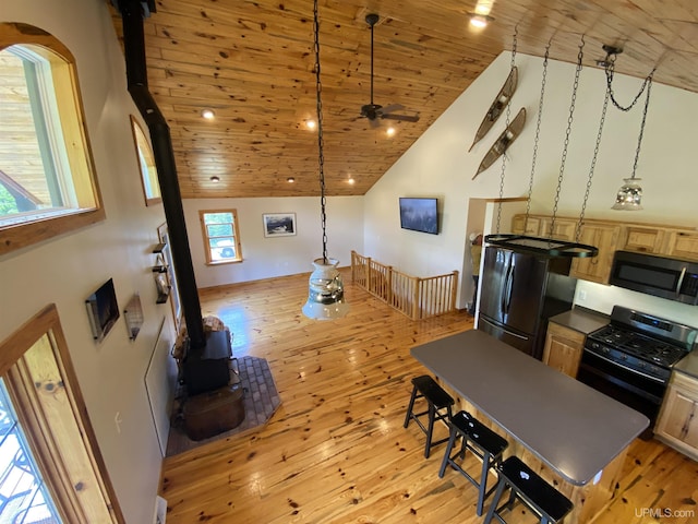 kitchen with light wood-style floors, a wood stove, high vaulted ceiling, wooden ceiling, and black appliances