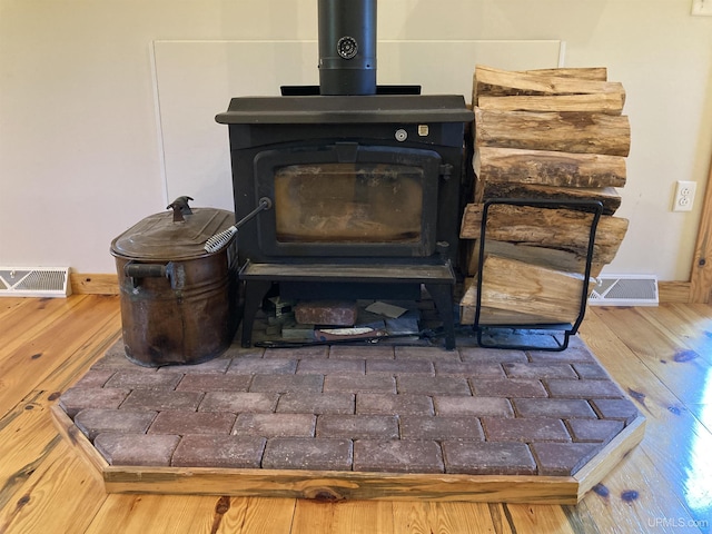 room details with visible vents, wood finished floors, a wood stove, and baseboards