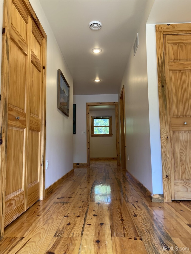 corridor with light wood-type flooring, visible vents, and baseboards