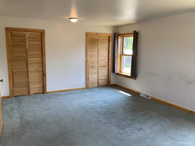 unfurnished bedroom with multiple closets, carpet, visible vents, and baseboards