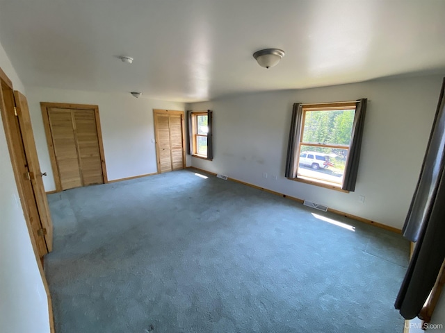 unfurnished bedroom with multiple closets, visible vents, carpet floors, and baseboards